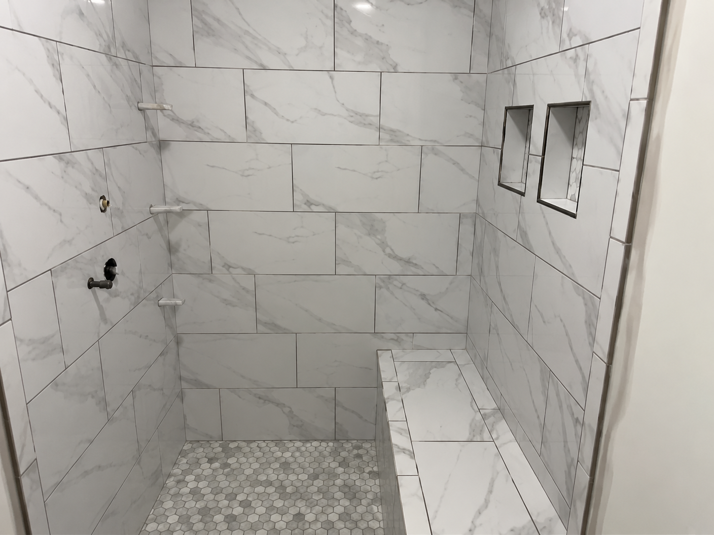 Marble-look tile shower with bench and niches